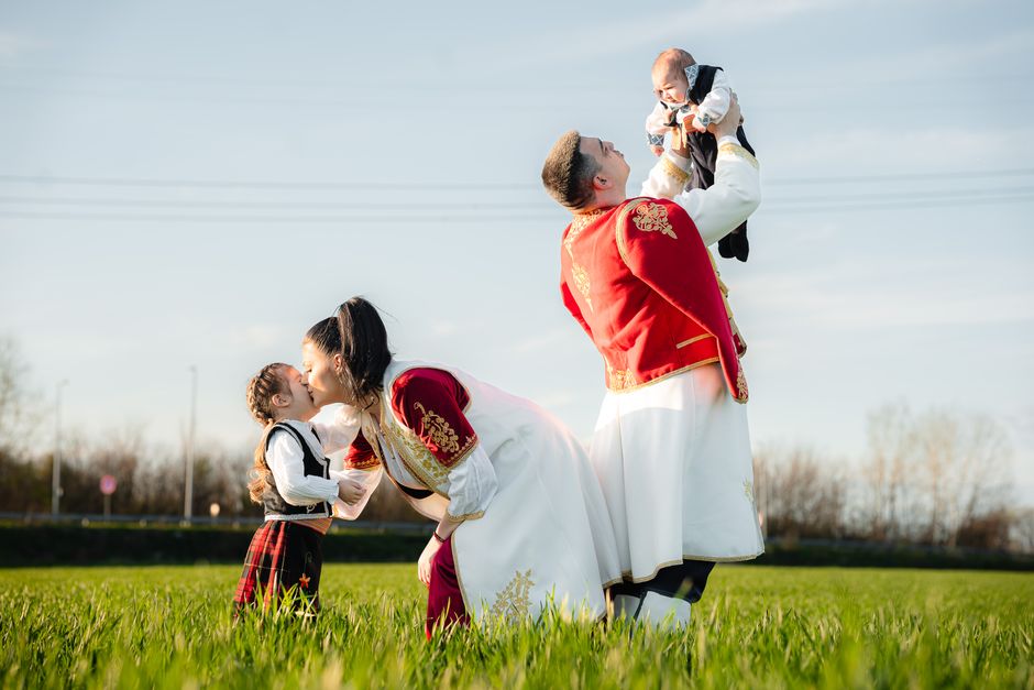 Joyful family in traditional attire playing in a sunny field, embracing cultural heritage.