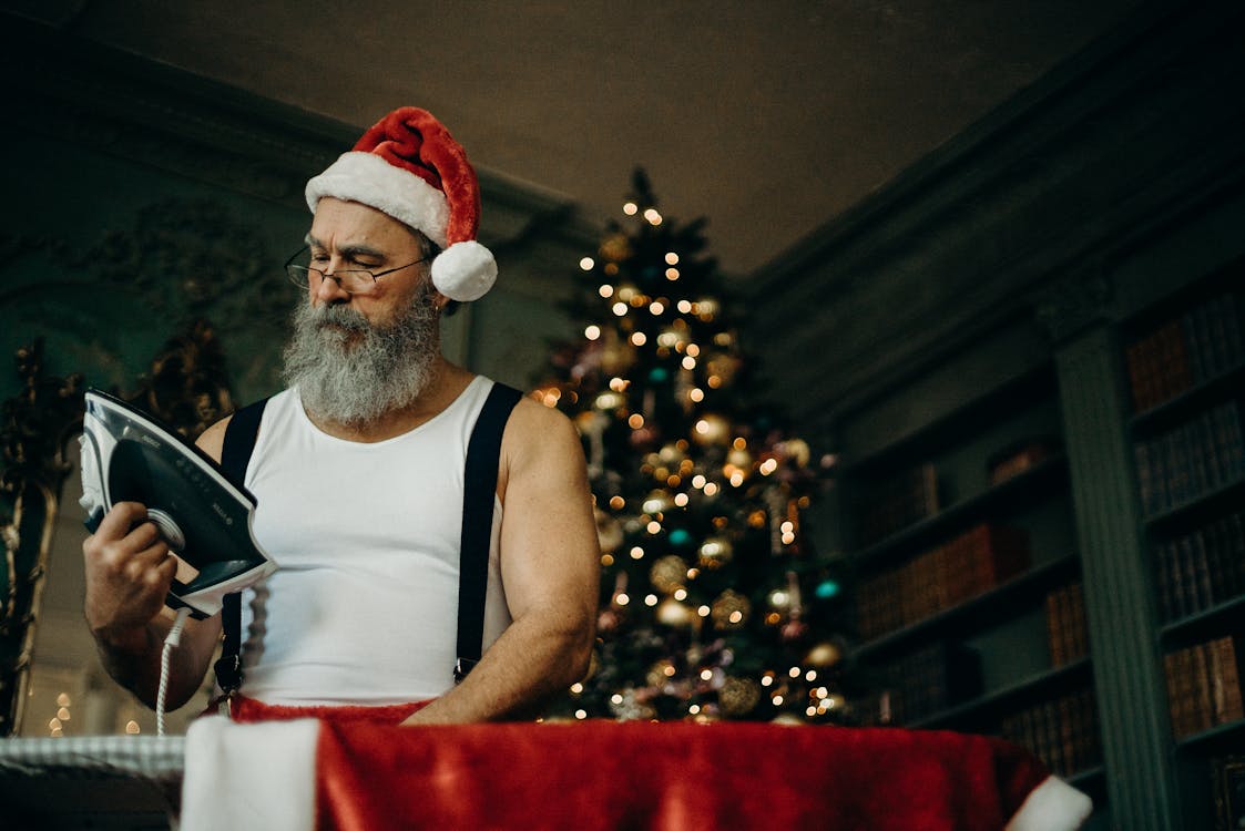 Free Man in White Tank Wearing Santa Hat Holding Black and Gray Dry Iron Stock Photo