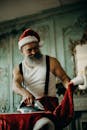 一位大胡子男人打扮成圣诞老人，在装饰房间里用温暖的微笑熨烫着他的服装