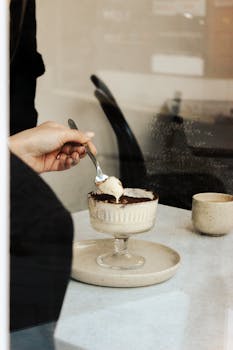 A person's hand enjoying a creamy dessert in a modern cafe, creating an inviting dining atmosphere.