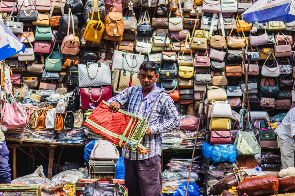 A street vendor showcases a variety of handbags at a bustling market in Kolkata, India.