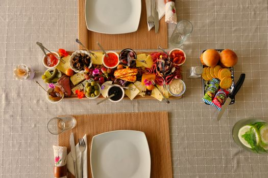 A colorful cheese and fruit platter with assorted cheeses, olives, and fresh fruit on a dining table setting.