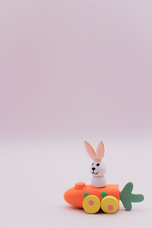 Free Adorable bunny figurine in a whimsical carrot-shaped toy car on a soft background. Stock Photo