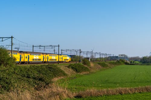 Free Vibrant yellow train travels through a scenic countryside with lush greenery on a sunny day. Stock Photo