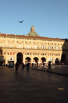 A vibrant and sunny view of Piazza Maggiore in Bologna, Italy, with people exploring the historic square.