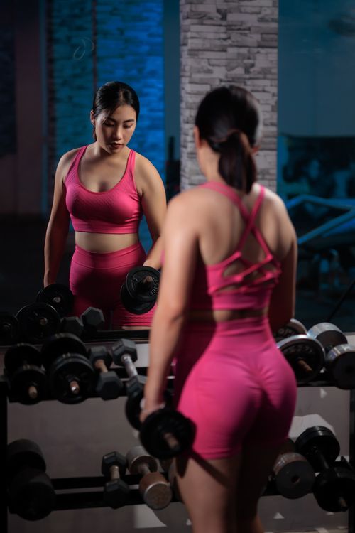 Free A woman in pink workout attire lifting dumbbells in a gym, focusing on strength training. Stock Photo