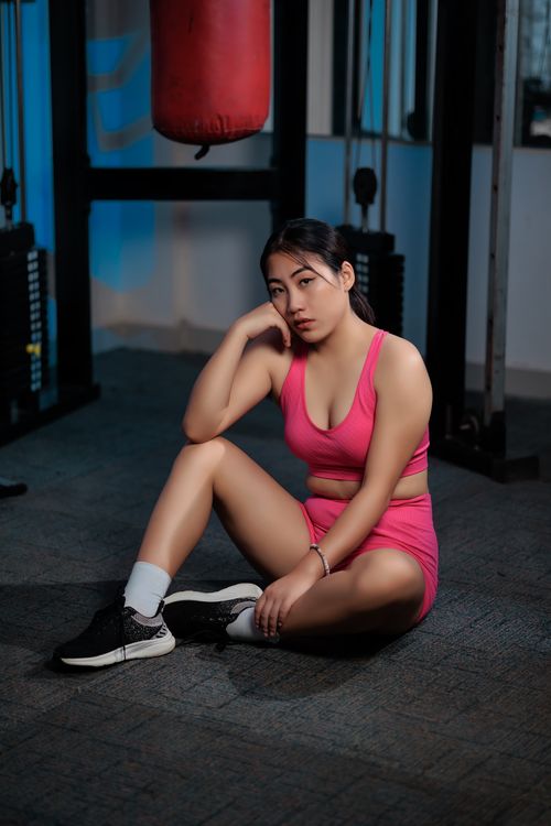 Free A woman in pink sportswear resting on the gym floor next to a punching bag, exuding determination. Stock Photo