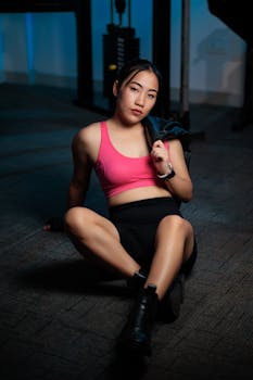 Young woman in sporty attire sitting on gym floor, resting between workouts.