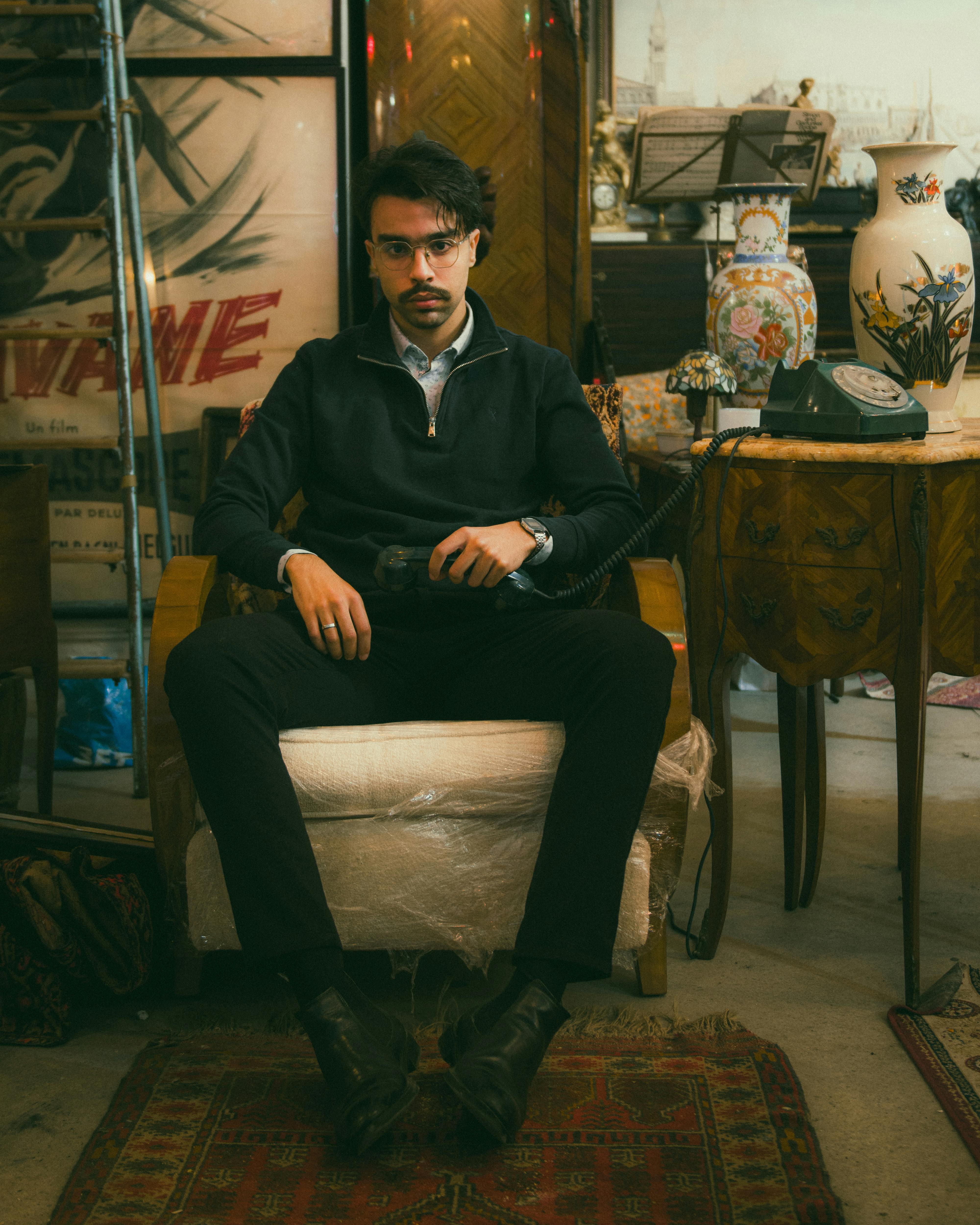 A stylish man dressed in vintage attire sitting in an antique store, exuding a classic 1920s mood.