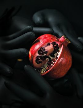 A vibrant pomegranate surrounded by mysterious black gloves.