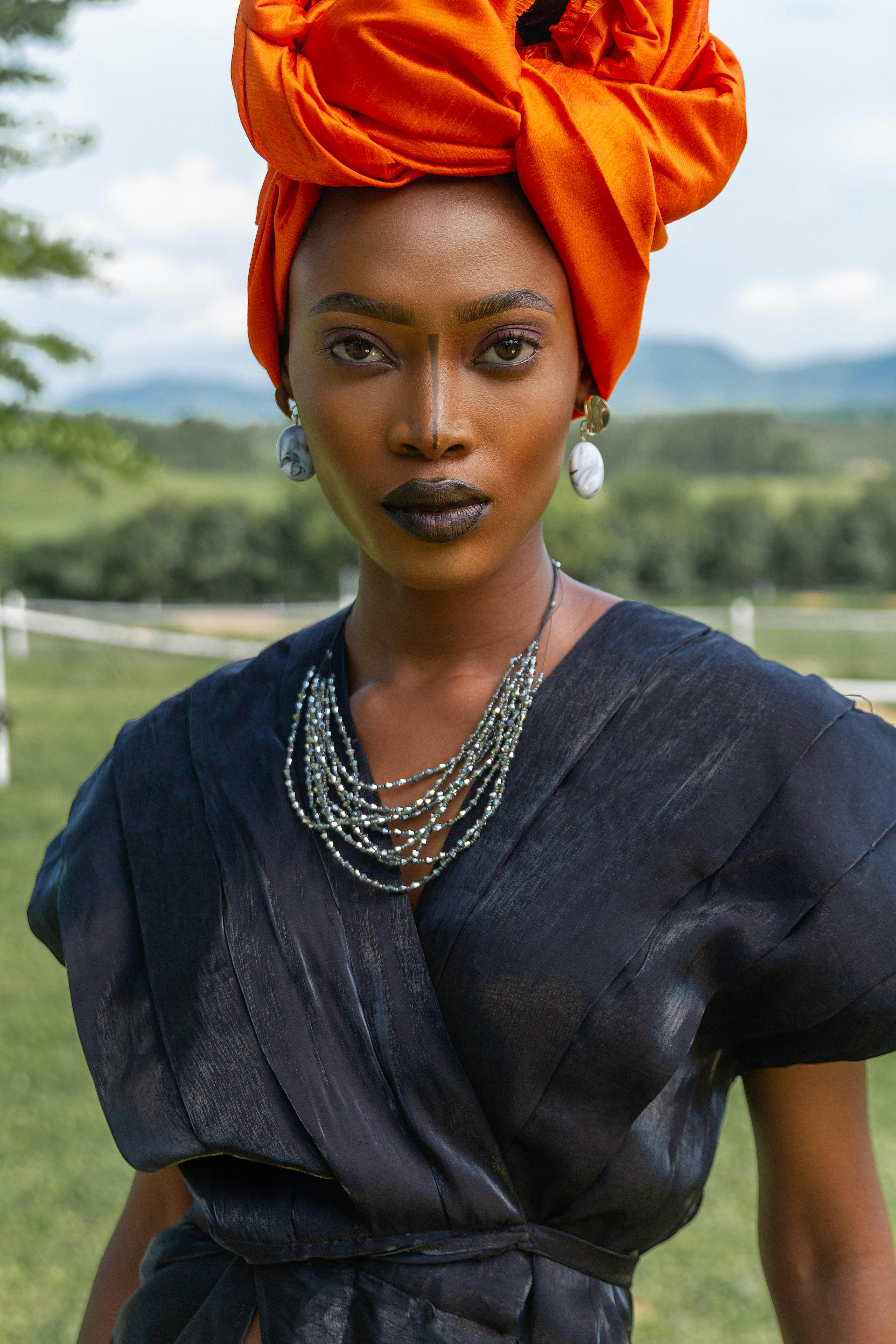 Stylish woman in a bold orange headwrap and black dress posing outdoors.