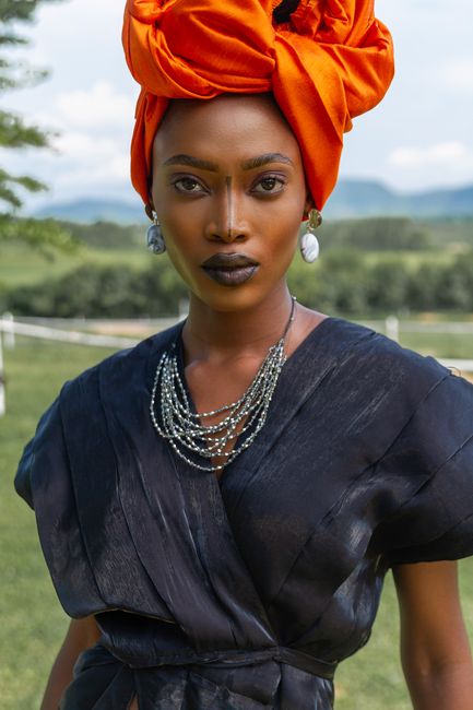 Stylish woman in a bold orange headwrap and black dress posing outdoors.