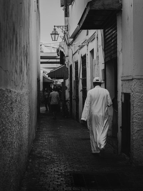 Free A man in traditional attire walks through a narrow historic street, creating a timeless scene. Stock Photo