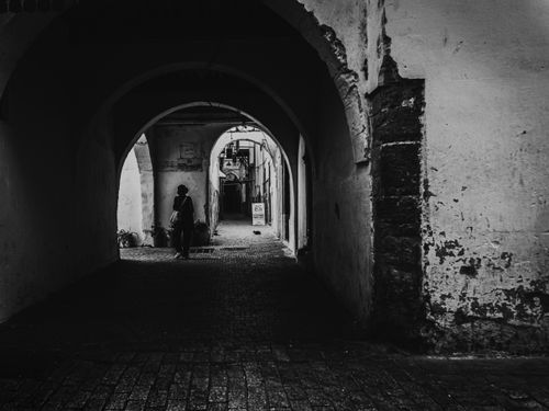Free A black and white photo of a person walking through an old archway, creating a mysterious and historic feel. Stock Photo