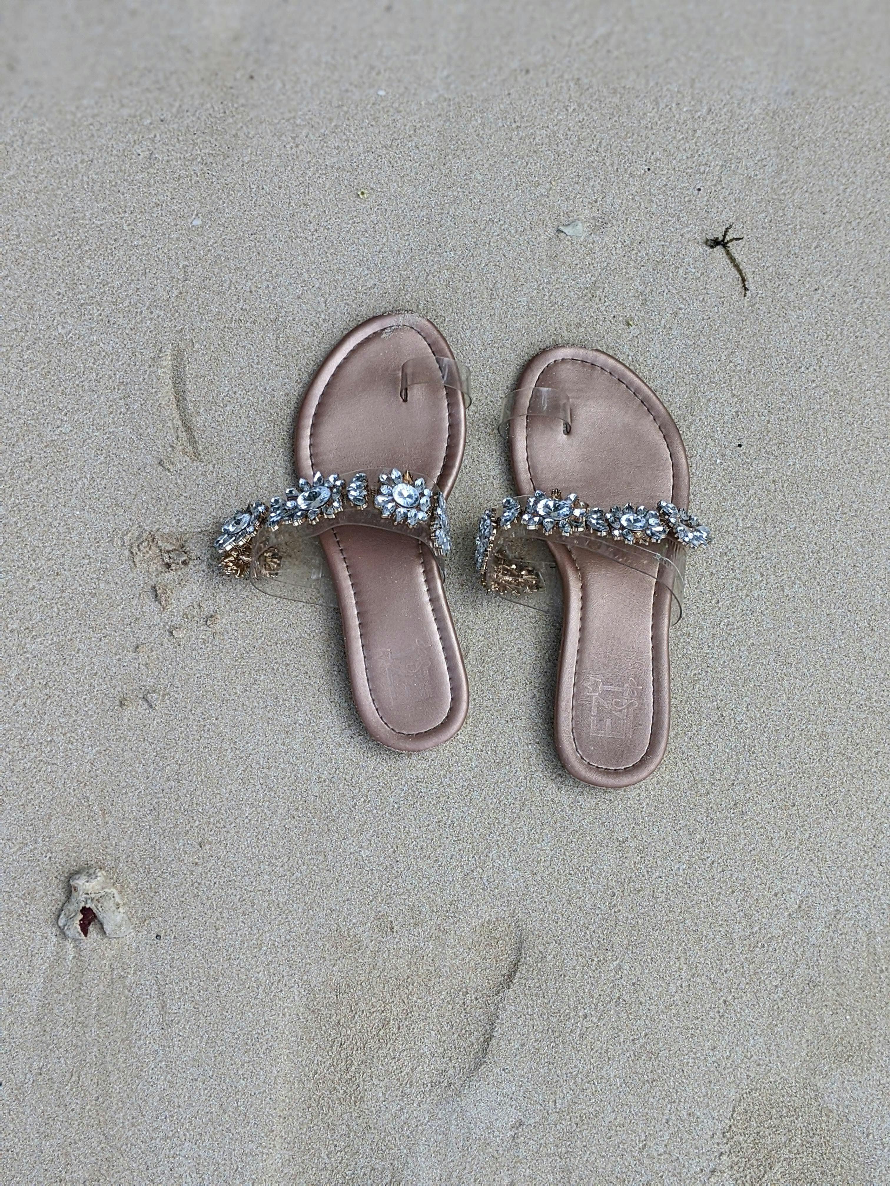 Free A pair of elegant, jeweled sandals resting on a sandy beach, suggesting a relaxed coastal vibe. Stock Photo