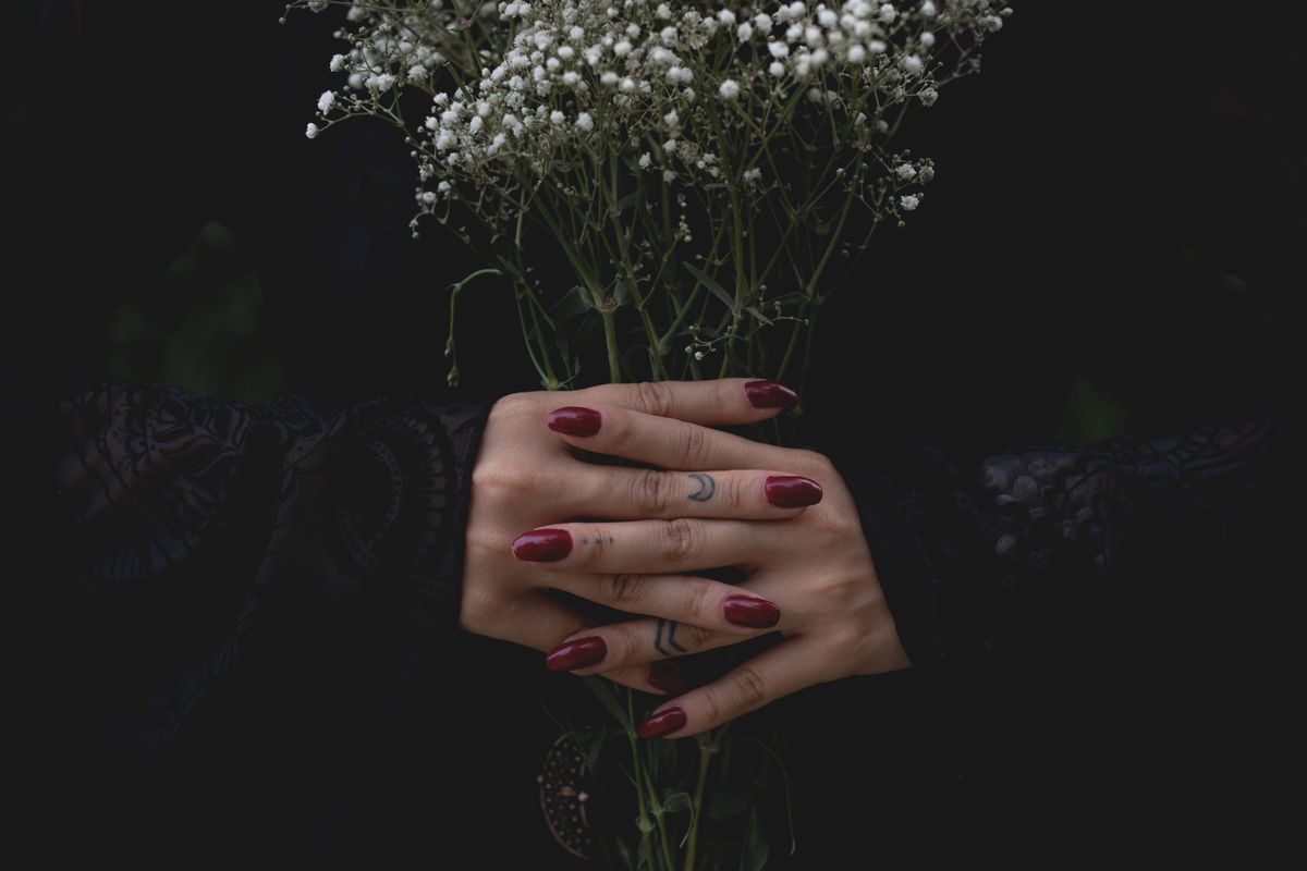 Elegant hands with red nails holding a bouquet of white gypsophila, evoking a mystical and serene vibe.
