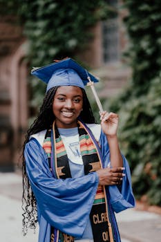 Happy graduate in blue cap and gown celebrating outdoors with diploma in hand.