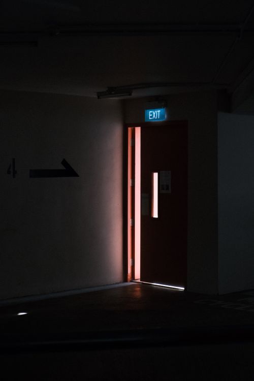 Free A partially open exit door with a glowing sign in a dimly lit corridor. Stock Photo