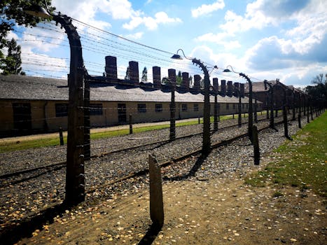 Barbed wire fence at a historical concentration camp with barracks in background.