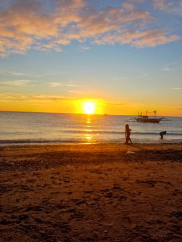 Serene sunset view over a beach in San Jose, Philippines, with boats and people enjoying the evening.