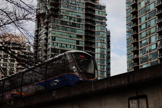SkyTrain passing modern high-rise buildings in Vancouver, emphasizing urban transit and architecture.