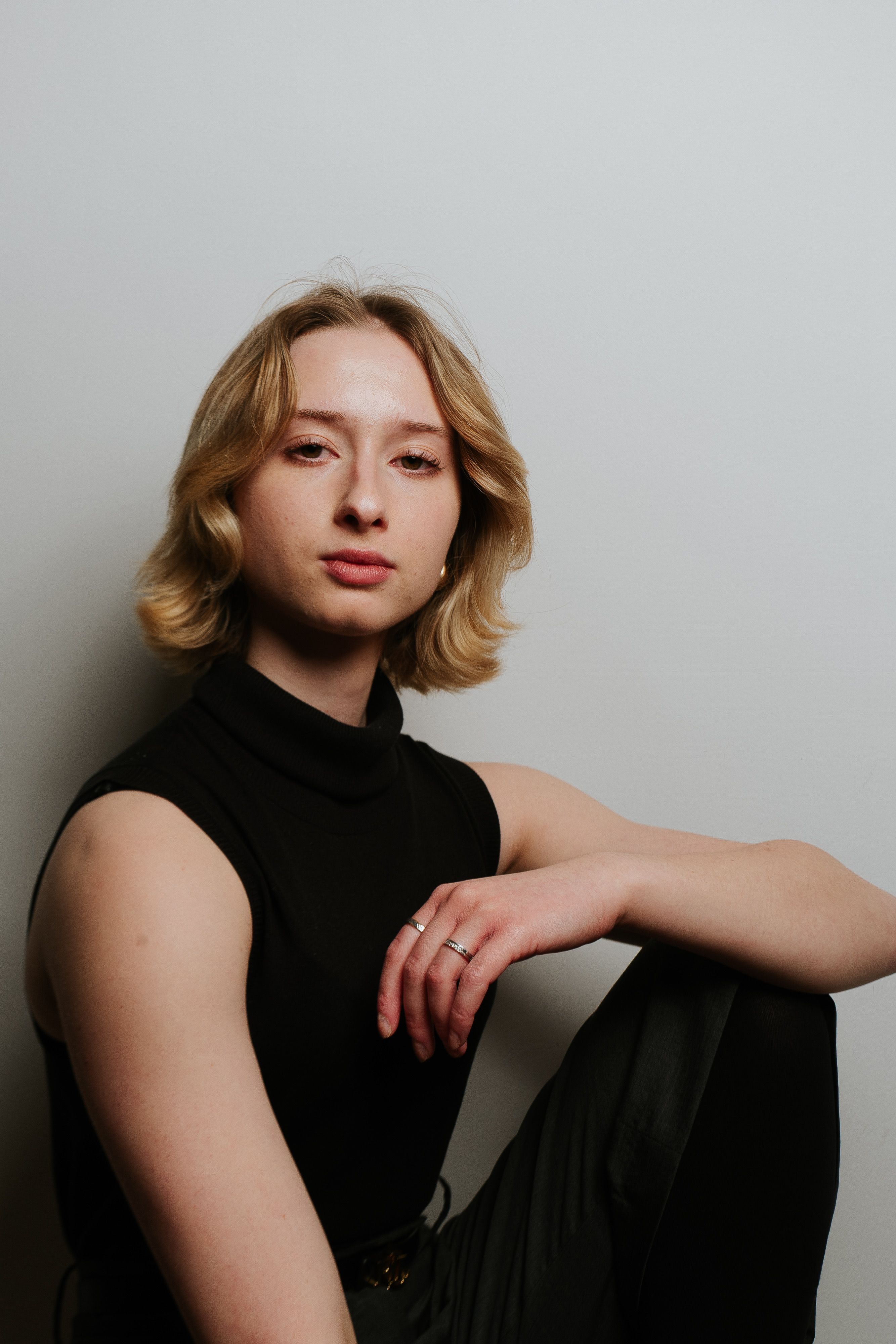 Portrait of a confident young woman in a black turtleneck against a neutral background.