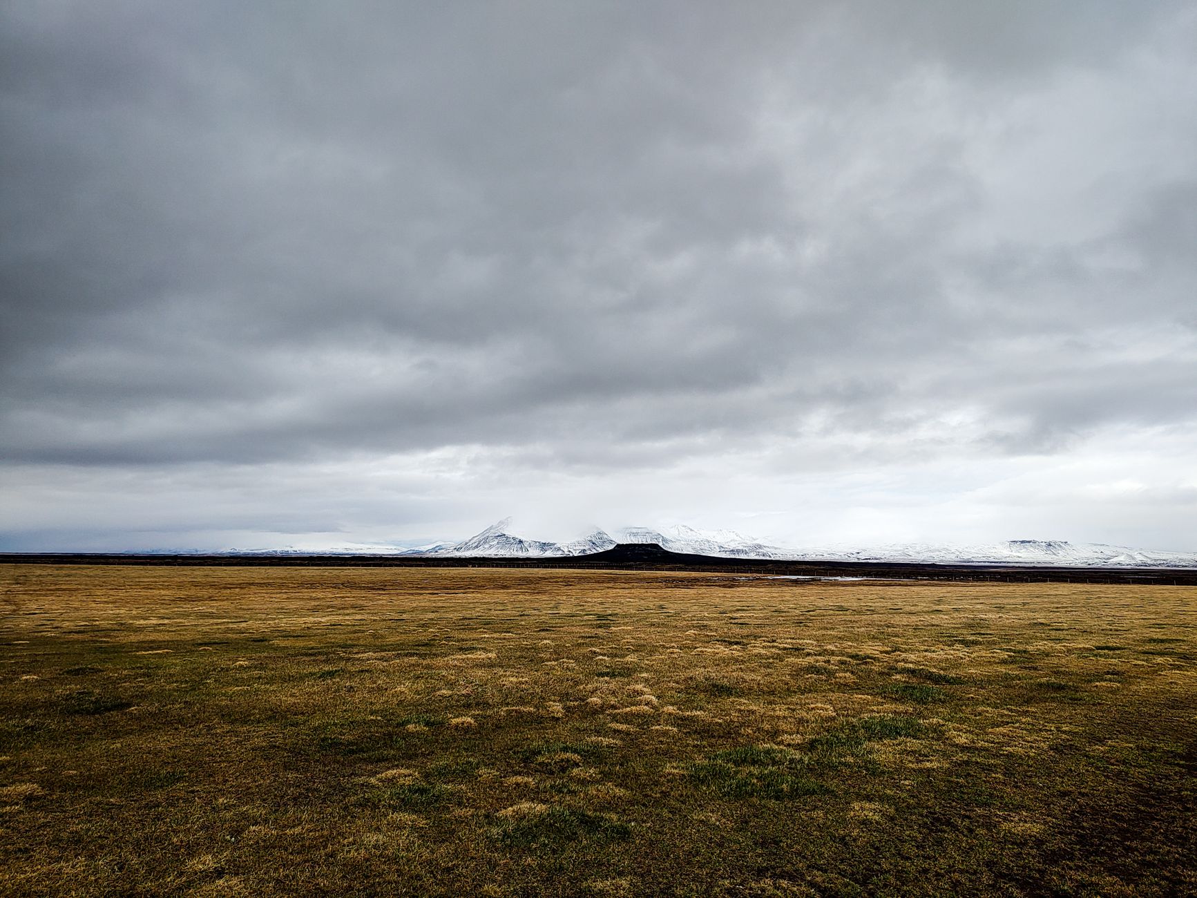 A wide Icelandic landscape with mountains under moody clouds, showcasing nature's dramatic beauty.