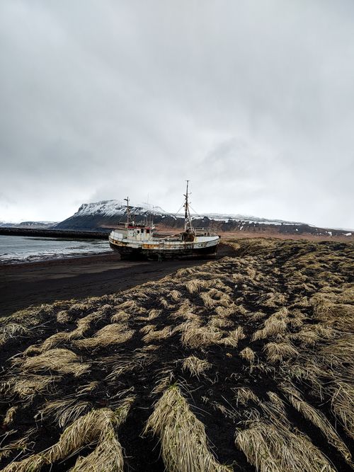 Free Rusty shipwreck on a dramatic black sand beach in Iceland surrounded by snow-capped mountains. Stock Photo