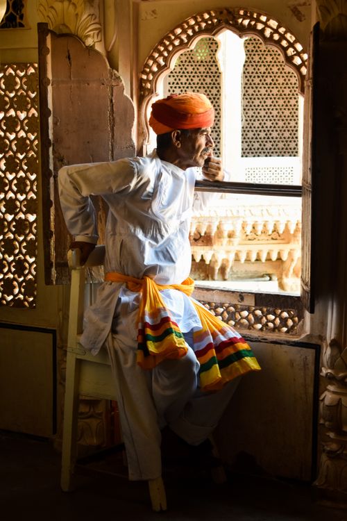 Free A Rajasthani man in traditional attire gazing out of an ornate window in Jodhpur, India. Stock Photo