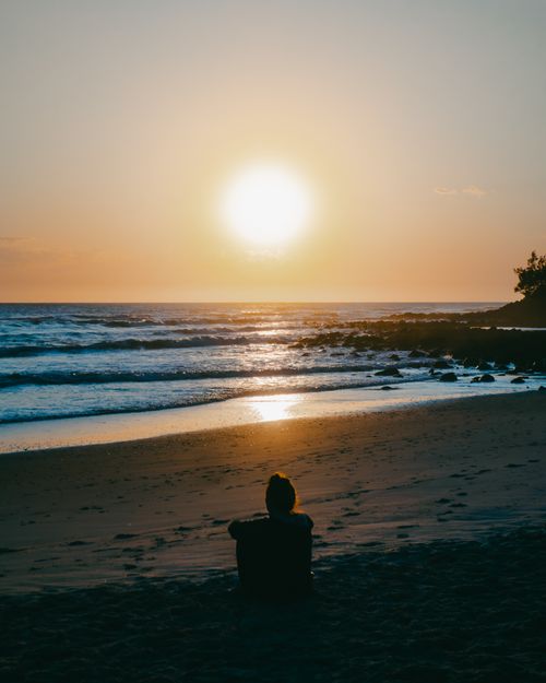 Free A peaceful sunset at Burleigh Heads Beach with a person sitting on the sand, capturing the tranquil ocean view. Stock Photo