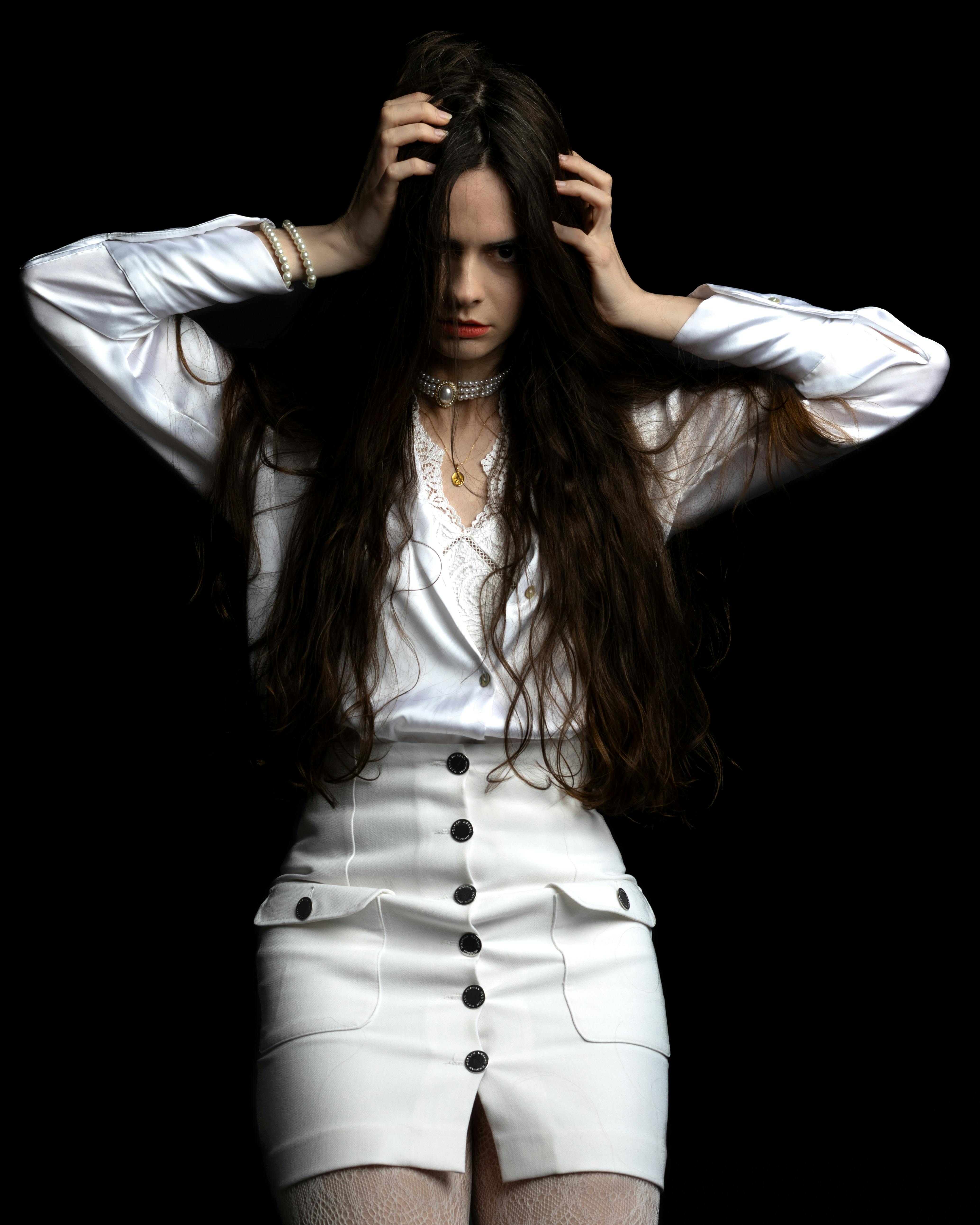 Free A striking portrait of a woman with long hair in a stylish white outfit against a dark background. Stock Photo