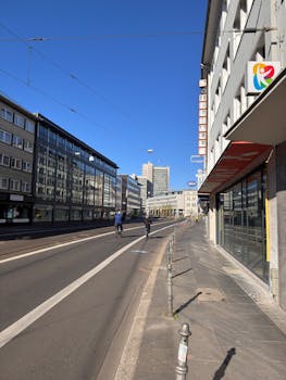 City street scene with cyclists, modern buildings, and a clear blue sky.