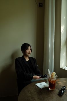Asian woman sitting in cafe with iced coffee, enjoying the afternoon light.