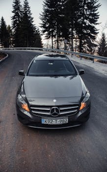 A sleek Mercedes-Benz parked on a winding forest road, framed by tall trees.