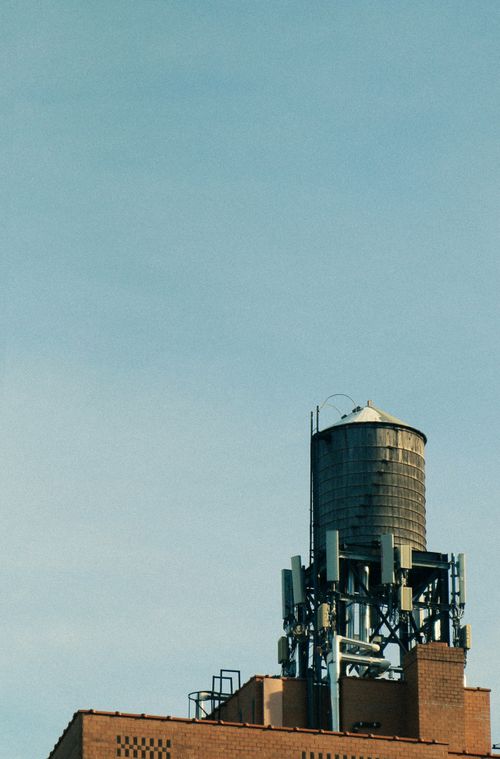 Free Vintage water tower on New York City rooftop under a clear blue sky, evoking a classic urban vibe. Stock Photo