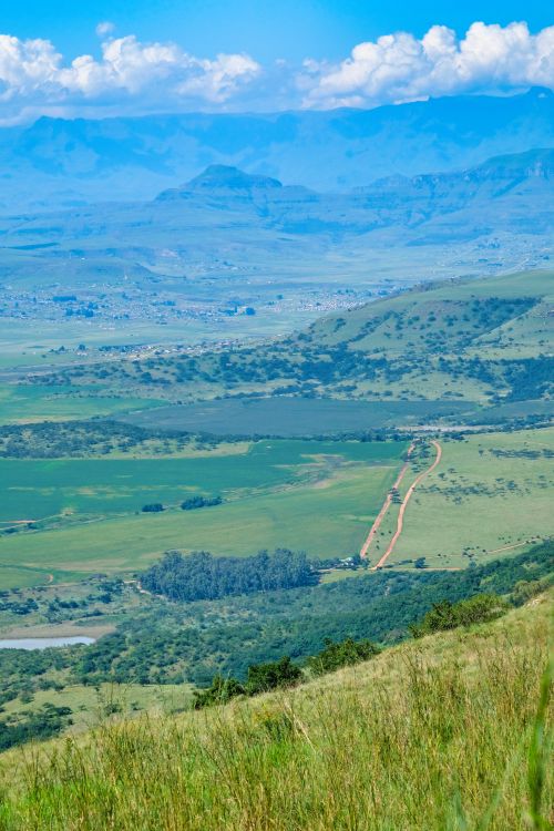 Free Stunning panorama of a lush green valley with distant mountains under a clear blue sky. Stock Photo