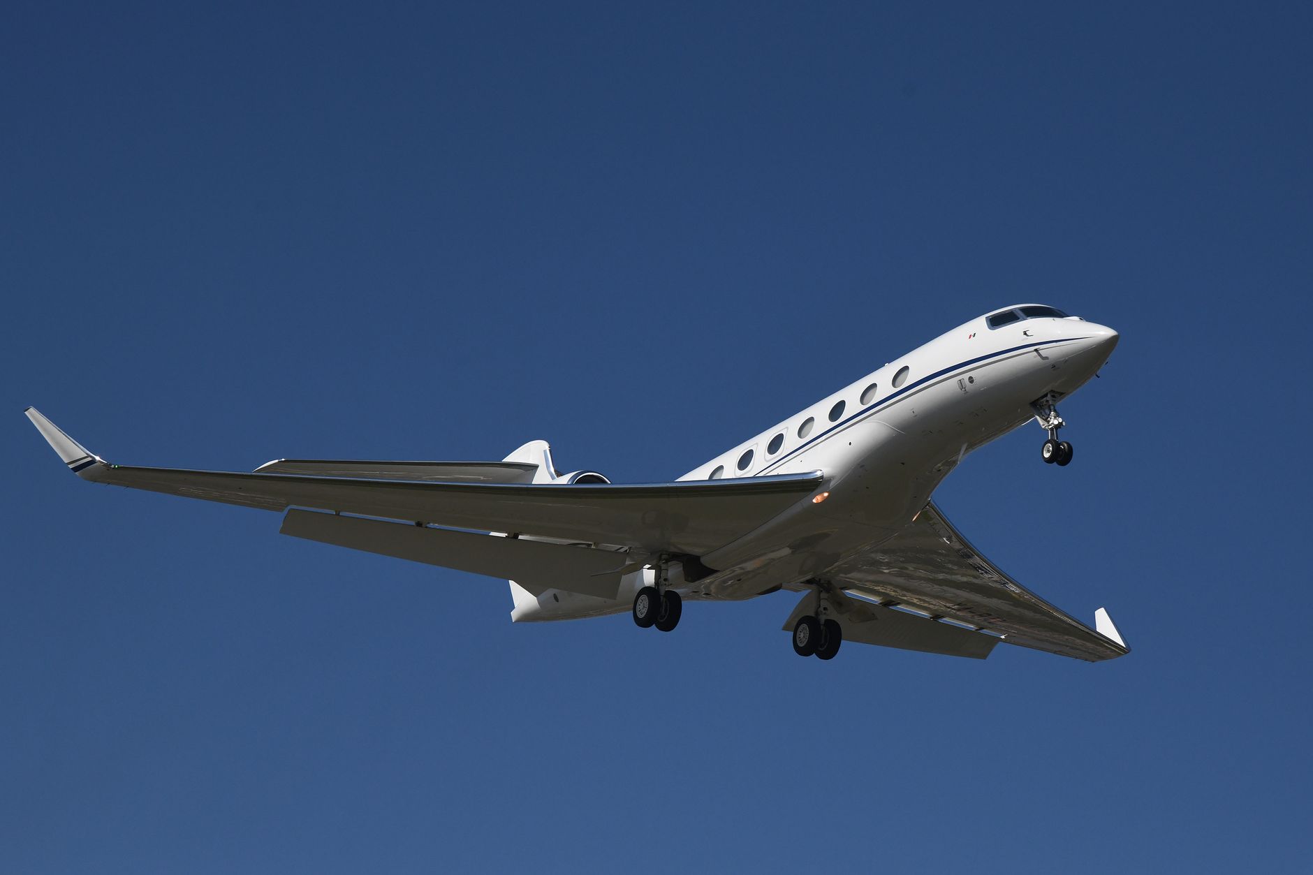 A sophisticated silver private jet soaring through a clear blue sky at high altitude during sunset.