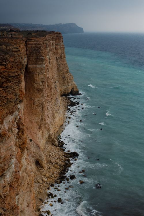 Free A scenic view of steep cliffs meeting the ocean under a dramatic, overcast sky. Stock Photo