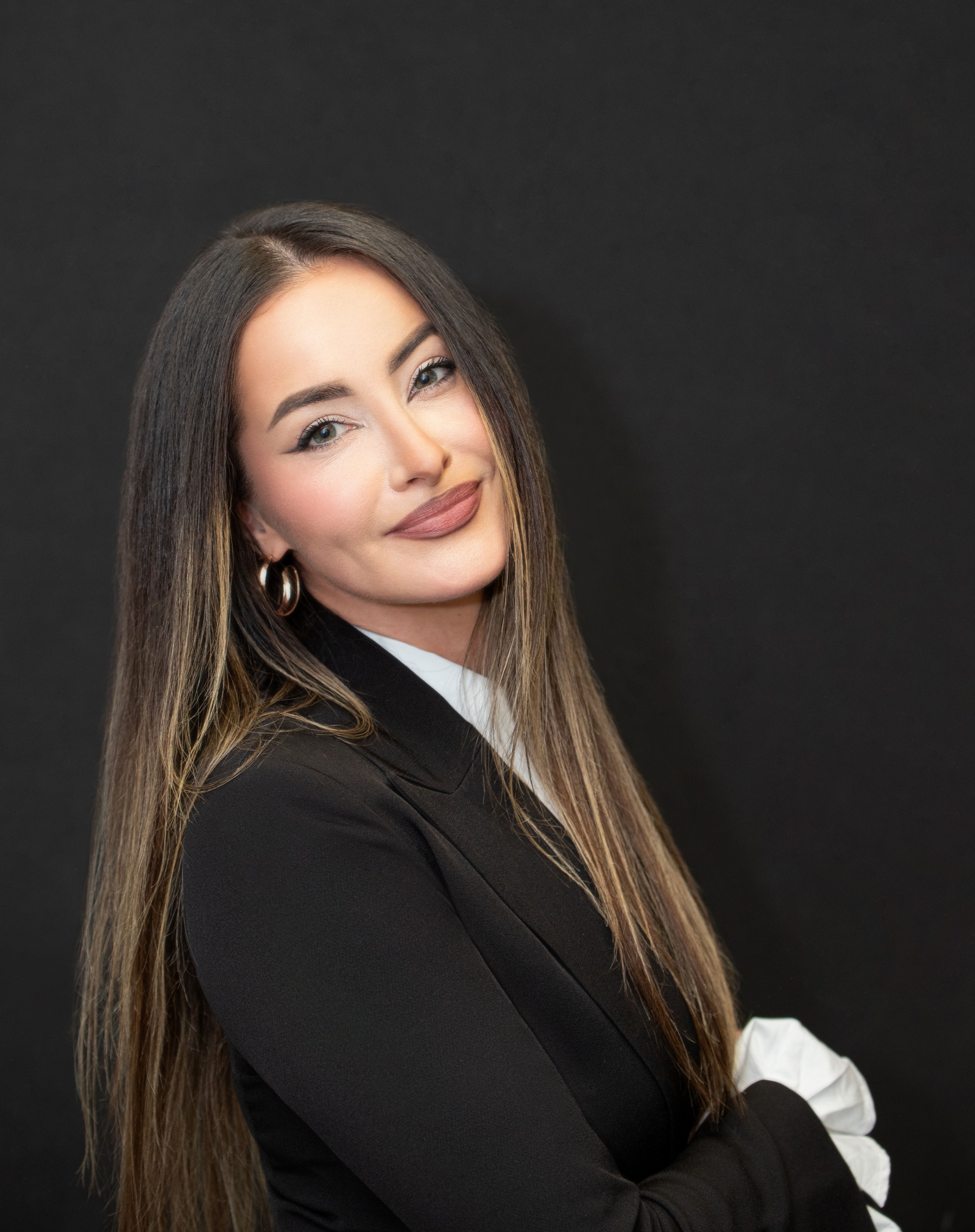 Portrait of a confident, well-dressed woman with long hair posing elegantly against a black background in Munich.