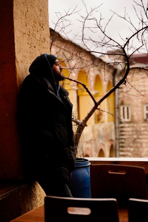 Free Man in hoodie leans against wall in a rustic outdoor scenic setting, lost in thought. Stock Photo