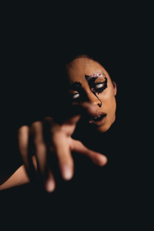 Free Moody portrait of a woman with eerie Halloween face paint reaching out in the dark. Stock Photo
