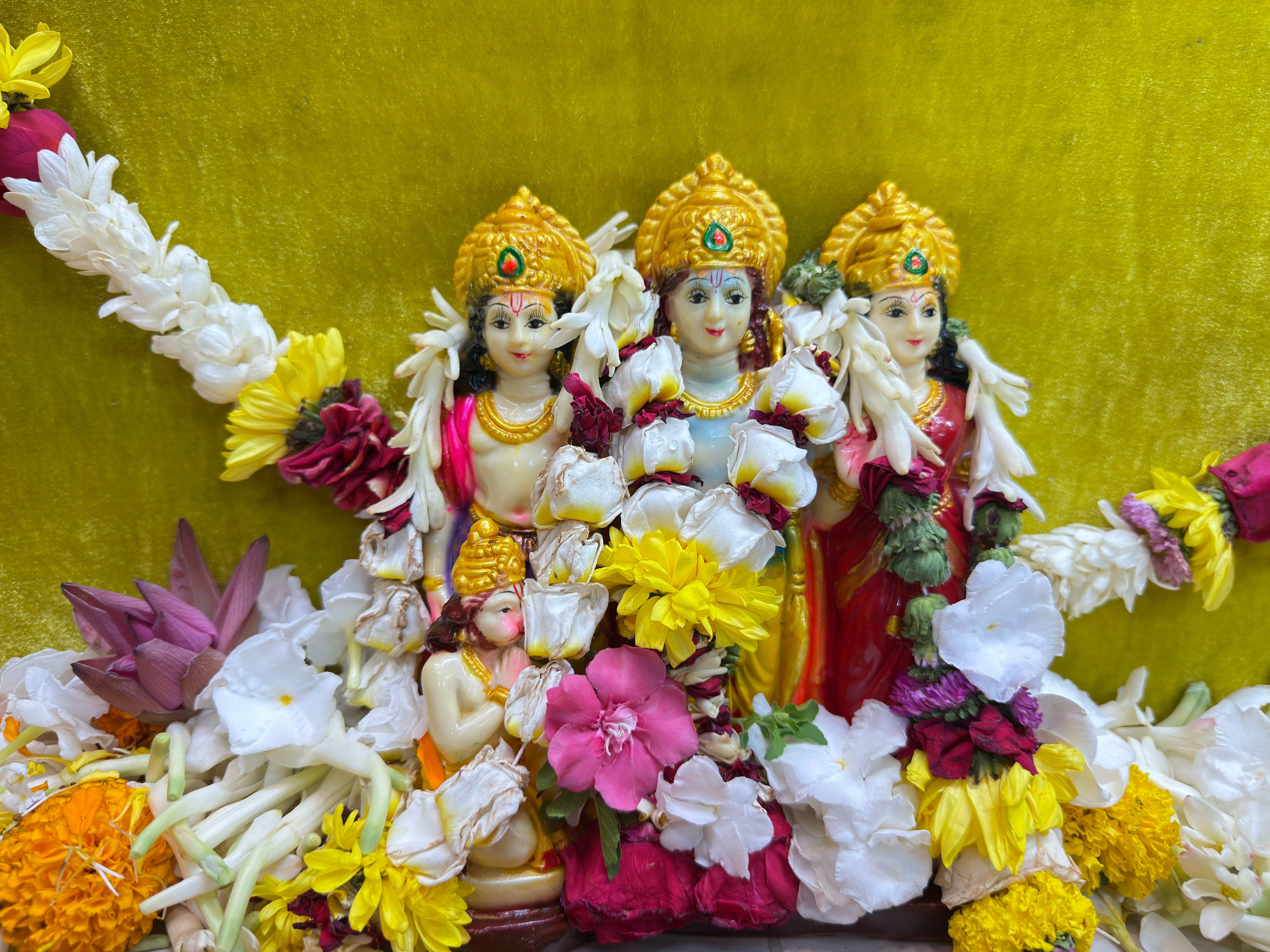 Intricately detailed Hindu deity statues adorned with colorful flowers on a vibrant backdrop.