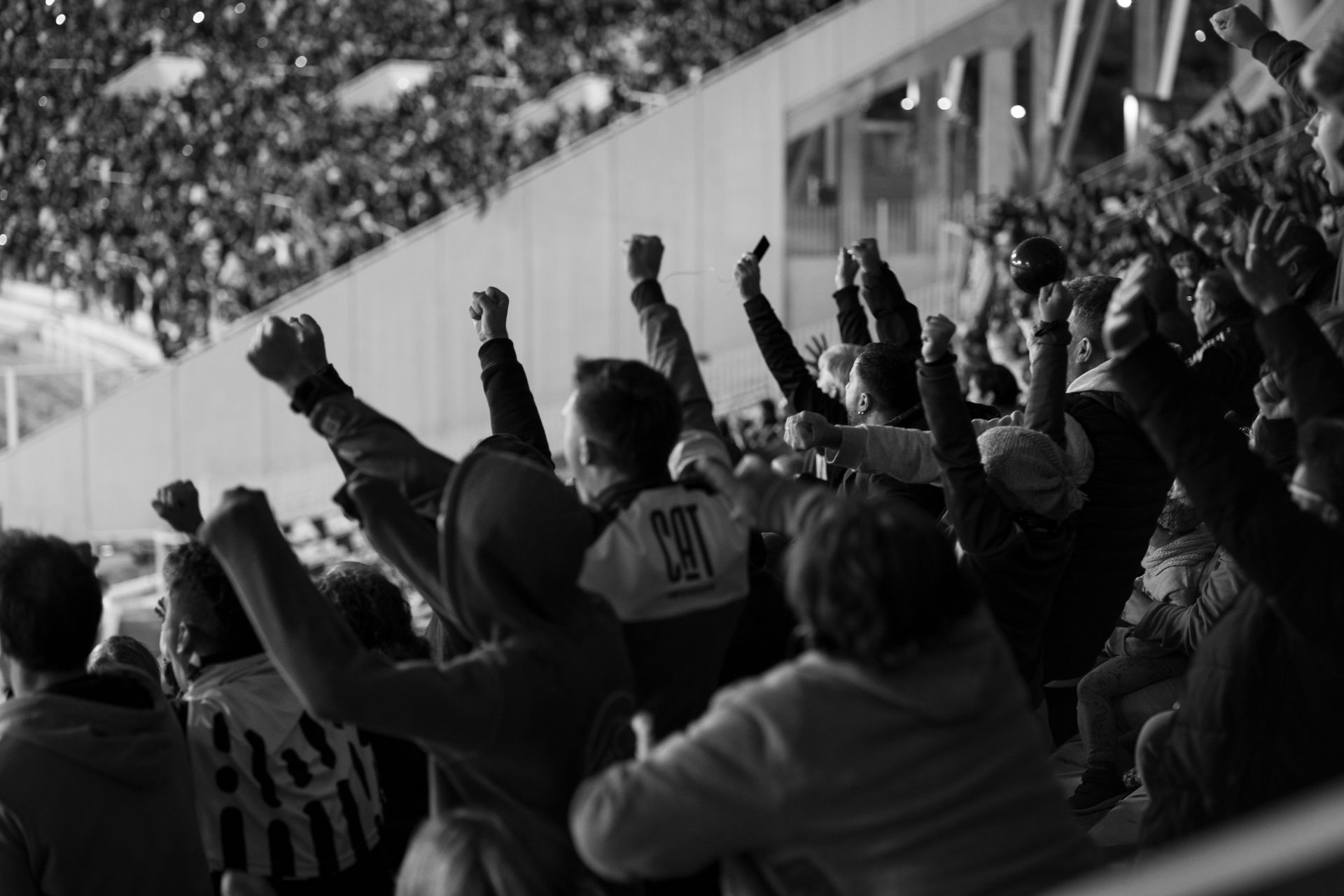 Black-and-white photo of football fans cheering in stadium stands, arms raised