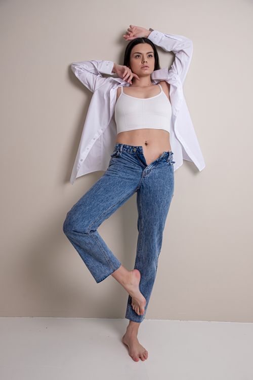 Free Young woman in casual pose against studio backdrop, wearing white top and jeans. Stock Photo