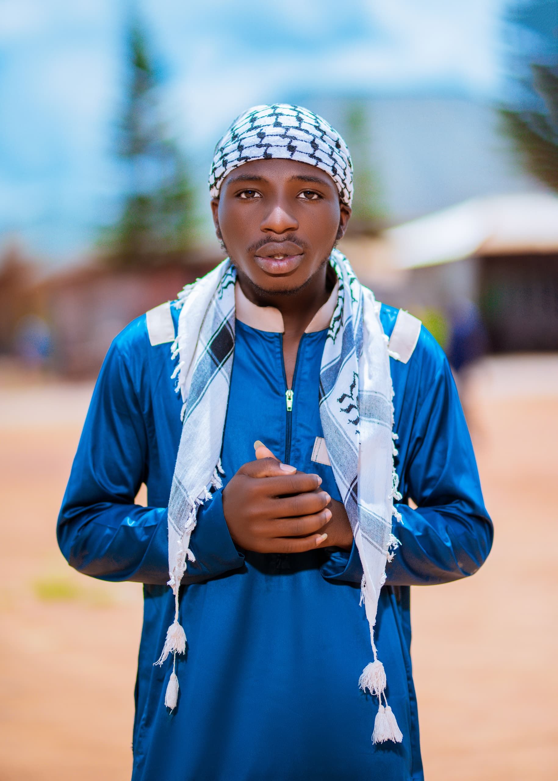Young man wearing traditional attire with a patterned scarf, standing outdoors.