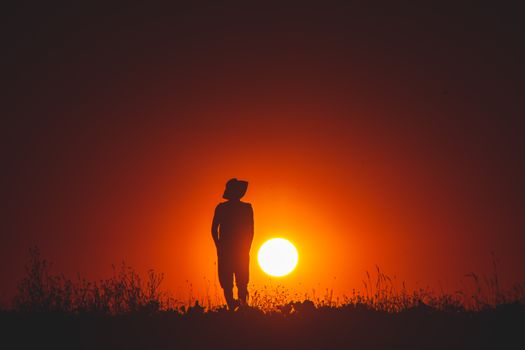 A captivating silhouette of a person in a field during a majestic sunset, casting a warm glow.