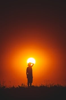 Silhouette of a person during a stunning sunset, with vibrant orange hues and a serene atmosphere.