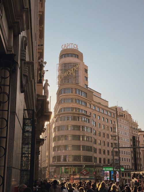 Free Vibrant street scene in Madrid, capturing the iconic Schweppes building on Gran Vía during sunset. Stock Photo