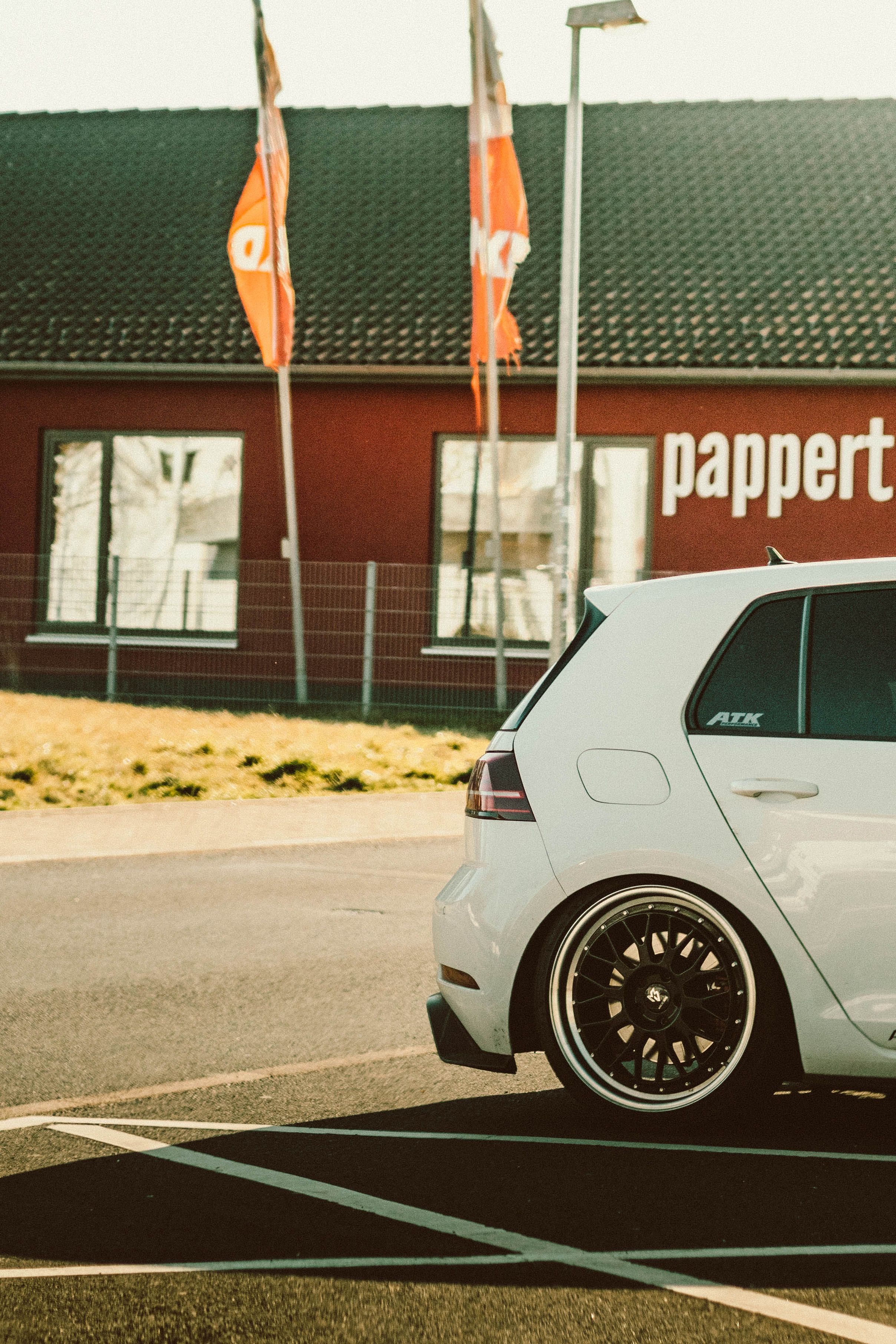 White Volkswagen Golf GTI parked in a lot near a building under a clear blue sky.