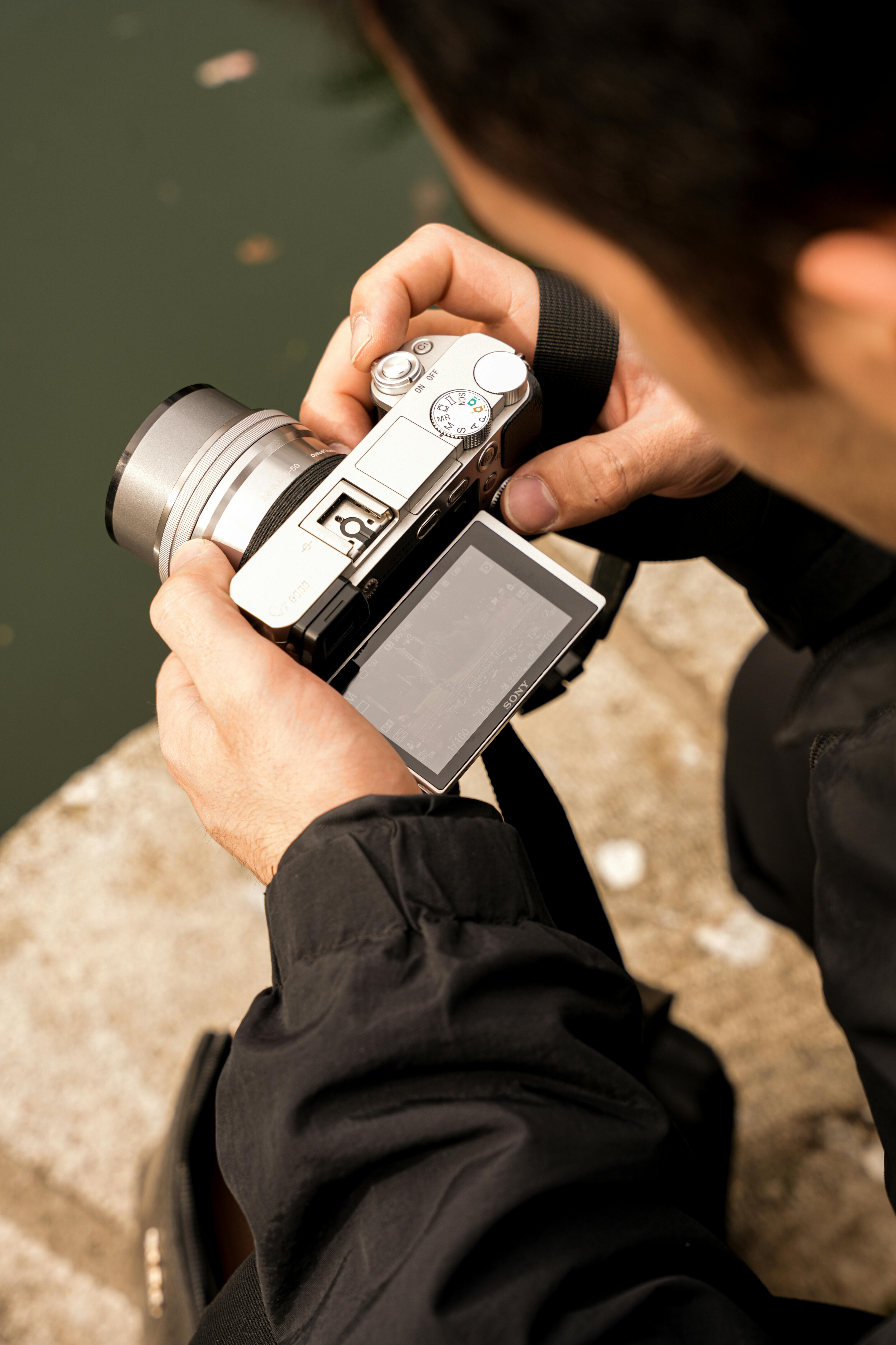 Detail osoby kontrolující fotografie na digitálním fotoaparátu venku.